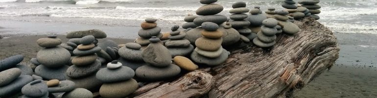 Smooth stones piled up on driftwood log on beach.