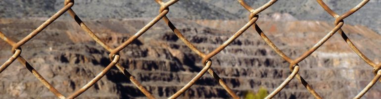 Rusty fence in foregroun; copper pit in background.