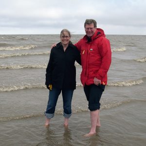 Two people in parkas standing barefoot in Arctic Ocean.